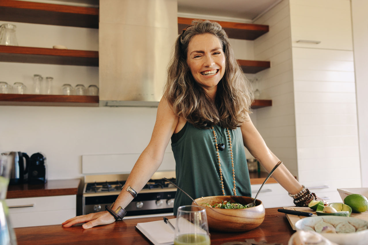 Woman in a kitchen with a bowl of salad, smiling.
