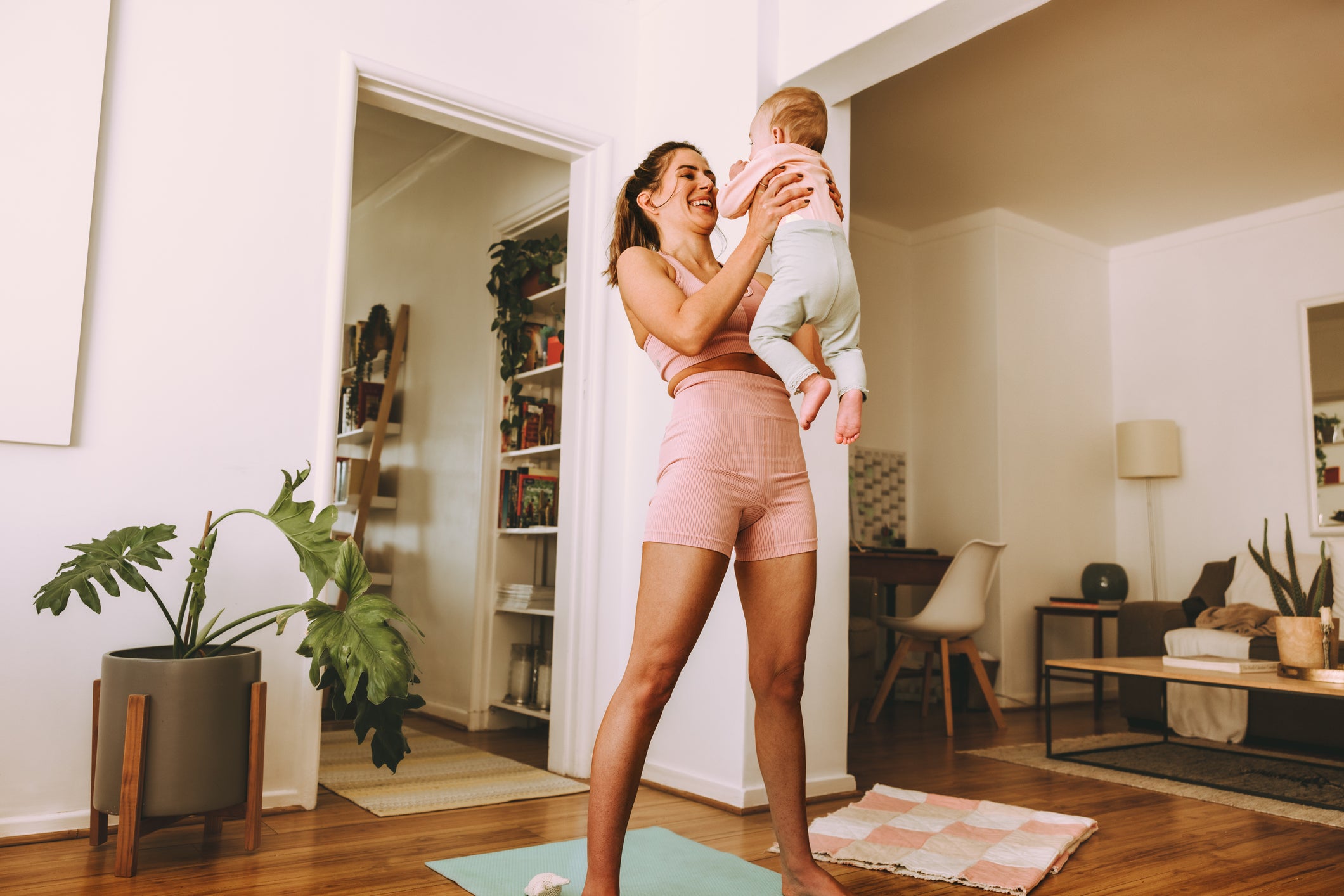 Woman in pink athletic wear holding a baby in a living room.