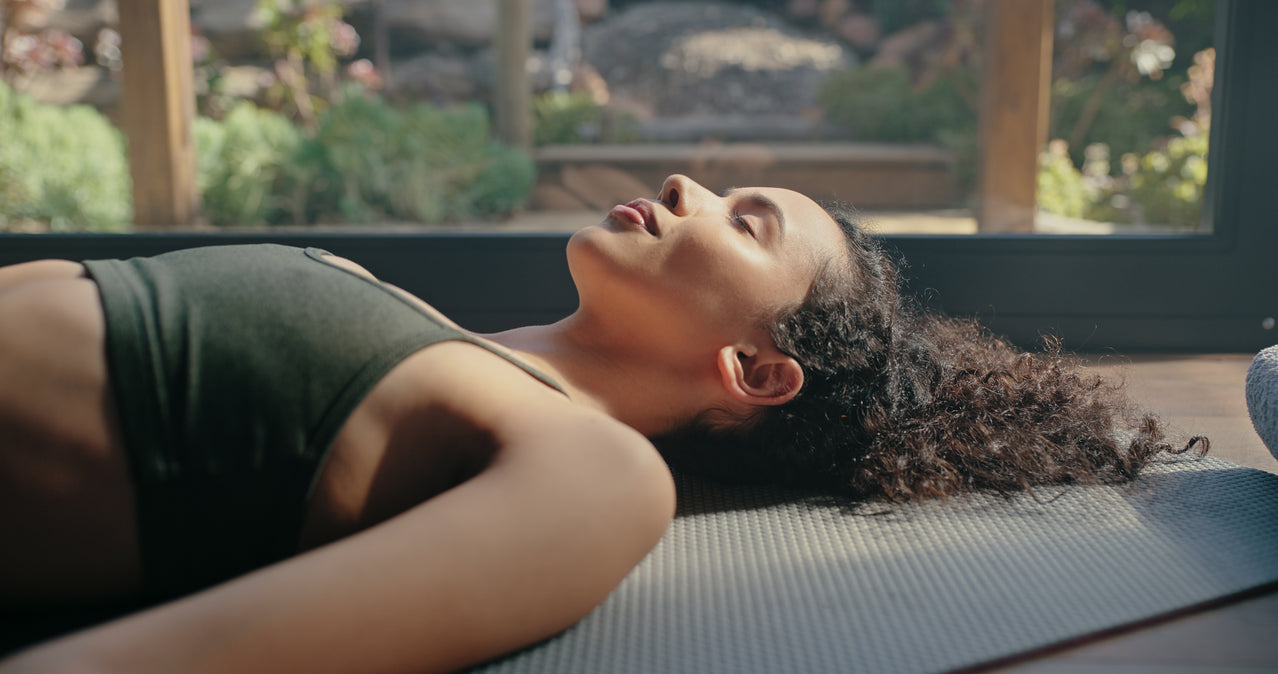 Woman lying on a yoga mat outdoors with a garden view