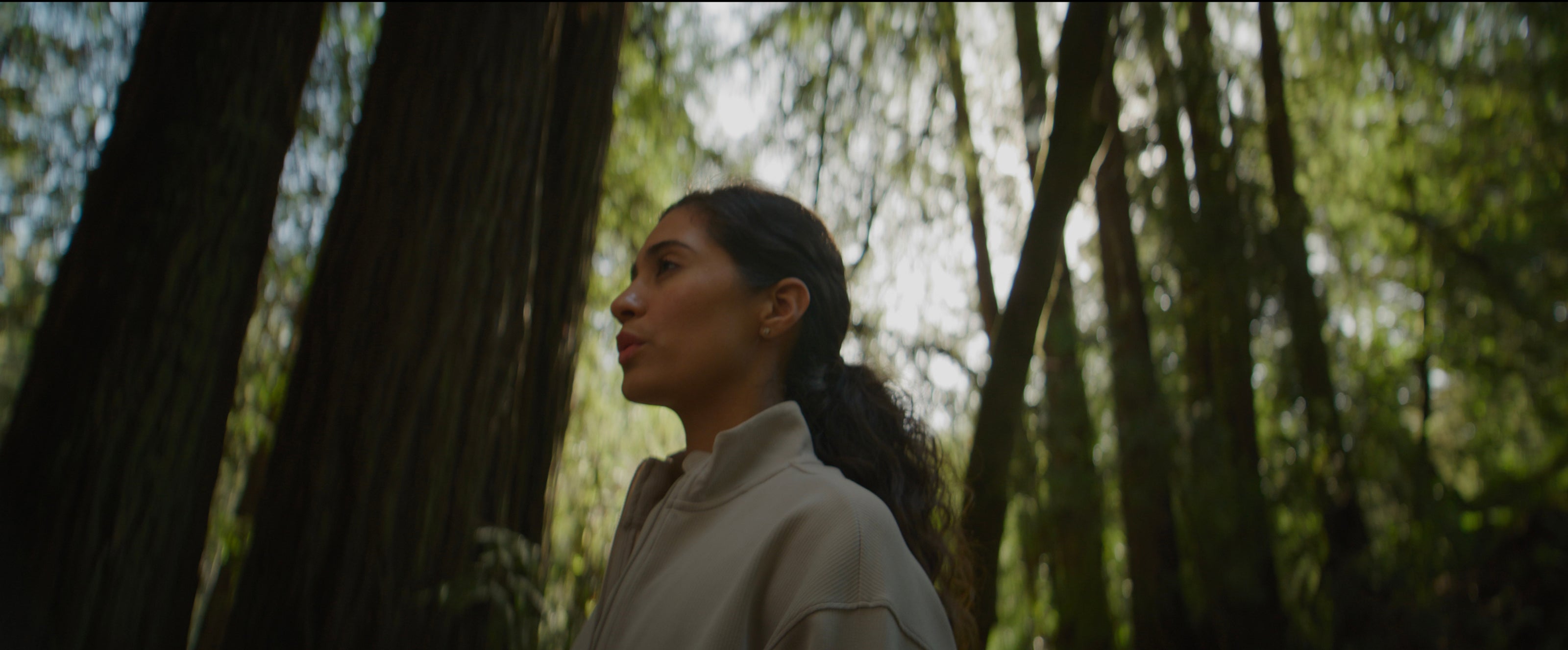 Woman standing in a forest with trees and greenery around her